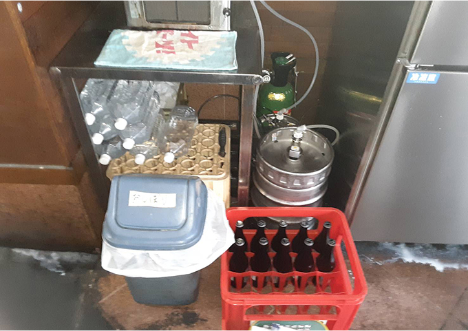 飲食店厨房の床に置かれた、清掃用品やゴミ箱、飲料ボトルの様子